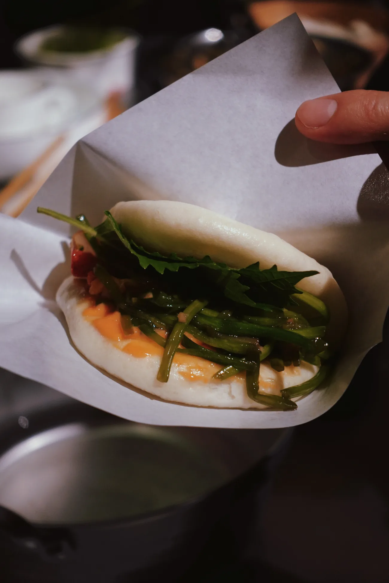 The finished bun in paper: shredded greens, chilli sauce, a leaf of shiso on top