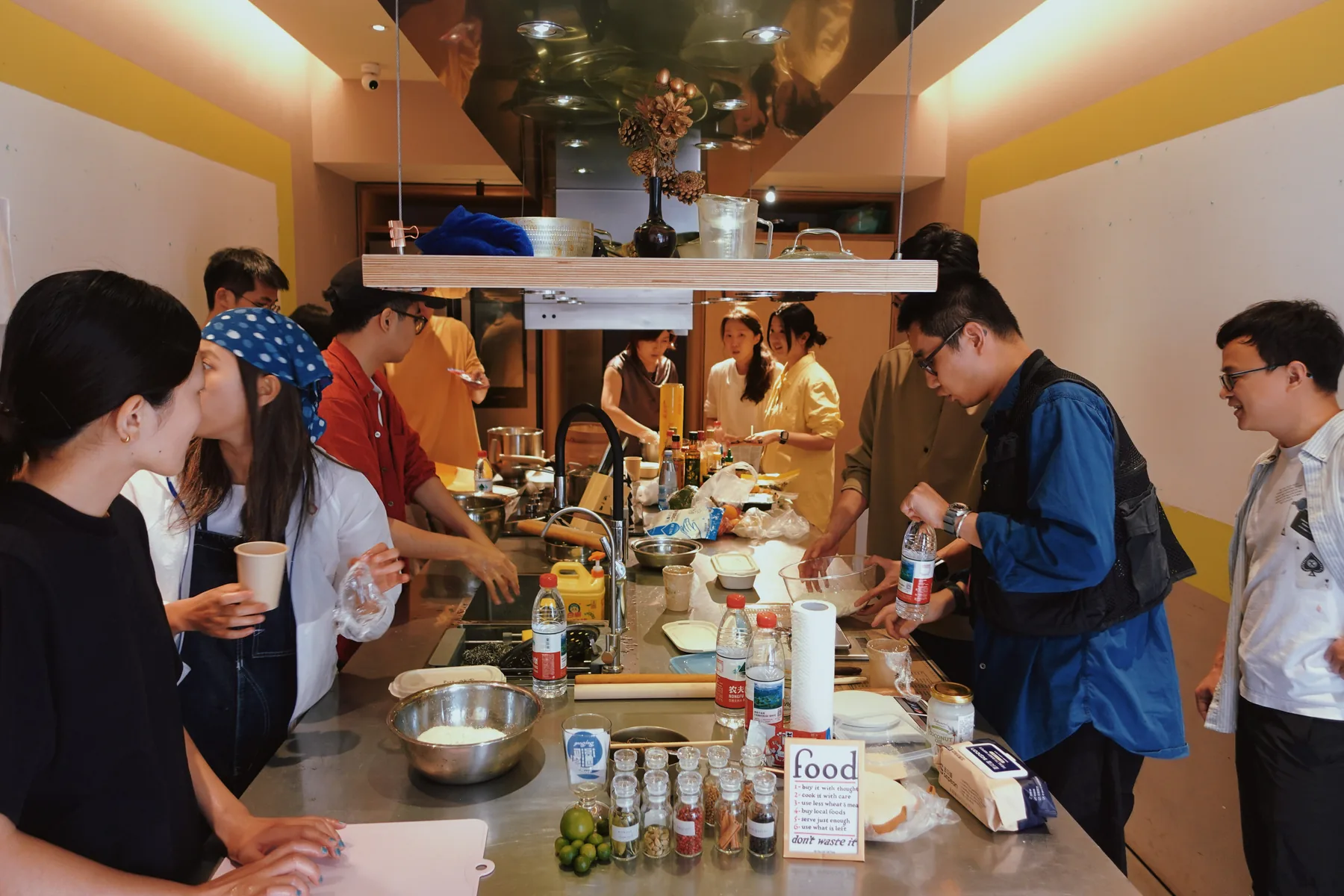The shared kitchen from one end: a long steel counter, the participants along both sides