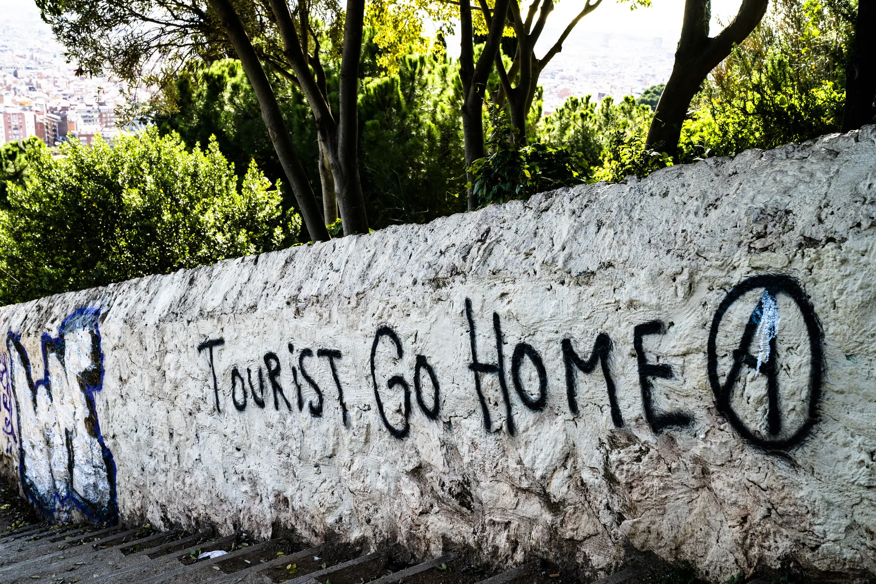 ‘Tourist Go Home’ painted on a whitewashed stone wall under trees